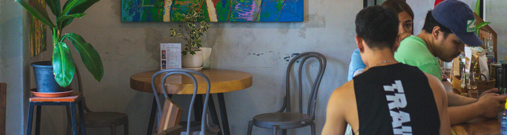 Inside-of-1AM-cafe-Koh-Samui-Thailand,-coffee-table-and-chair,-two-men-and-one-lady-sitting-at-table-counter
